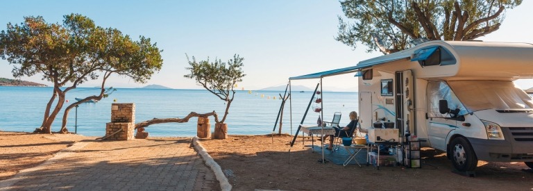 Familie die met een camper reist, eet ontbijt op een strand.