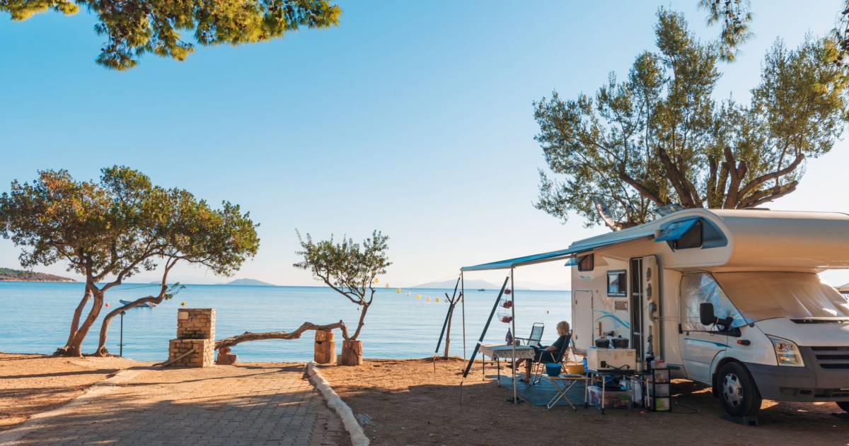 Familie die met een camper reist, eet ontbijt op een strand.